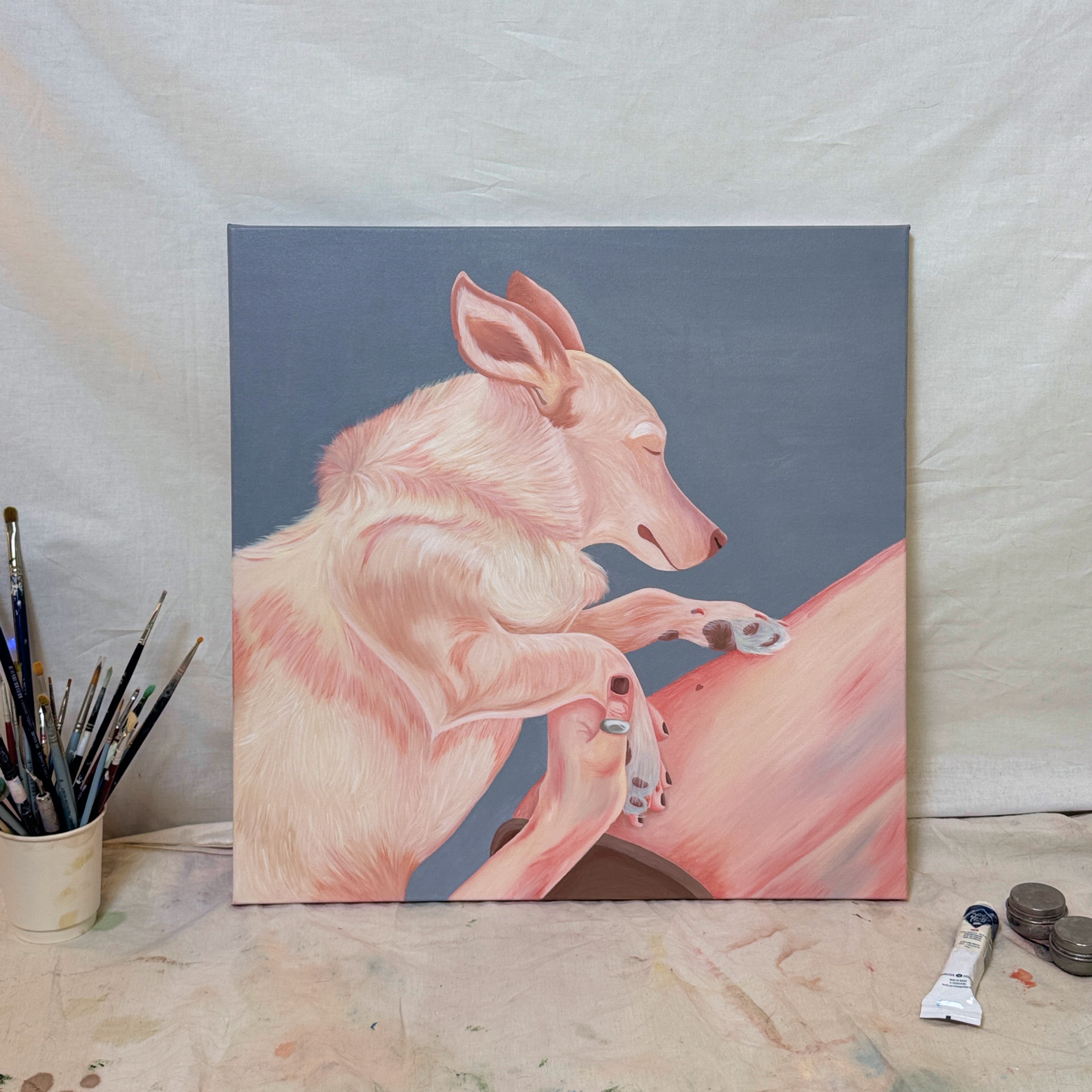 Картина маслом на холсте, изображающая светло-розовую собаку с закрытыми глазами, опирающуюся лапами на розовую форму на сине-сером фоне, стоит на светлой драпированной поверхности в студийном пространстве, рядом слева стакан с кистями, справа тюбики с краской, на фоне белой ткани